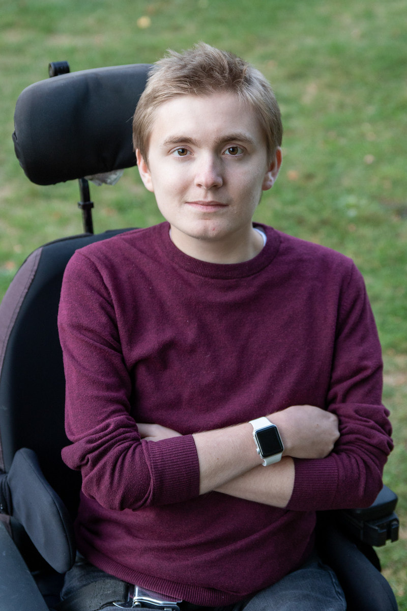 close up of Jake Marrazo seated outside in his powerchair with his arms crossed smiling at the camera.