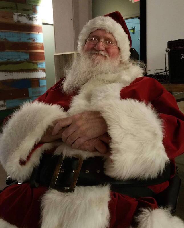 Santa smiling at the camera sitting with his hands crossed over his belly